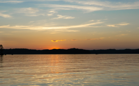 A body of water with trees and a sunset in the background.