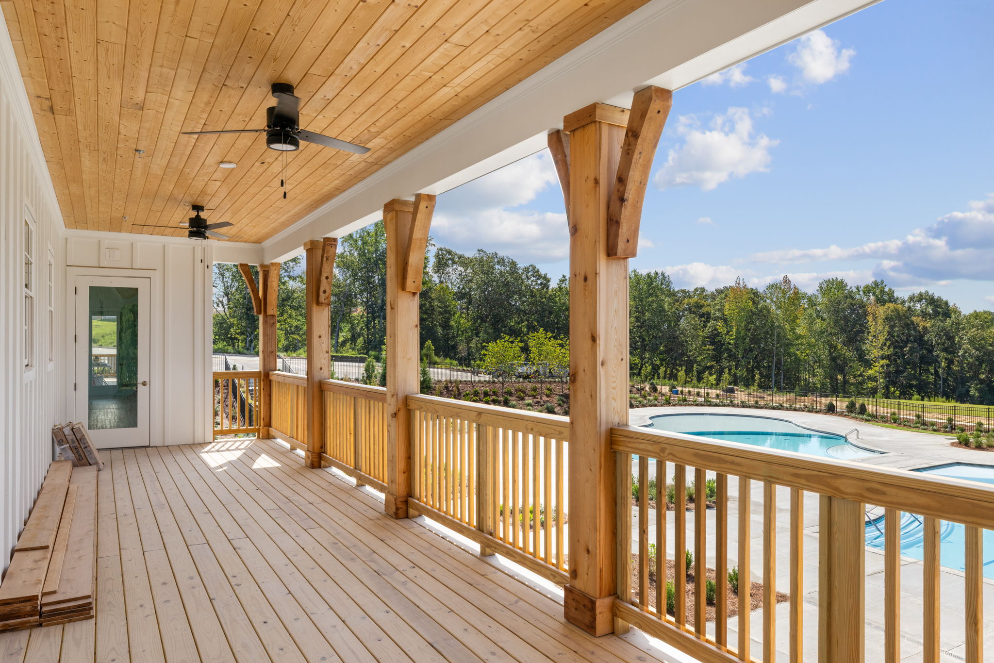 A deck with a pool and a wood railing with trees in the background.