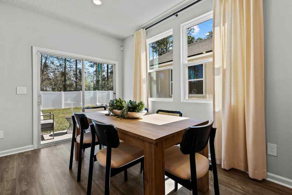 Davor Model Paired Home Dining Room with Wood Table and Black Chairs in Front of Patio Door at The Landings at Pecan Park