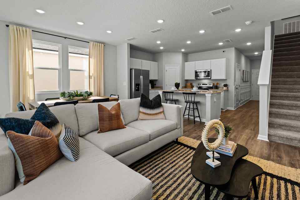 Davor Model Paired Home Living with Cream Couch Looking over Kitchen with White Cabinets and White Staircase at The Landings at Pecan Park