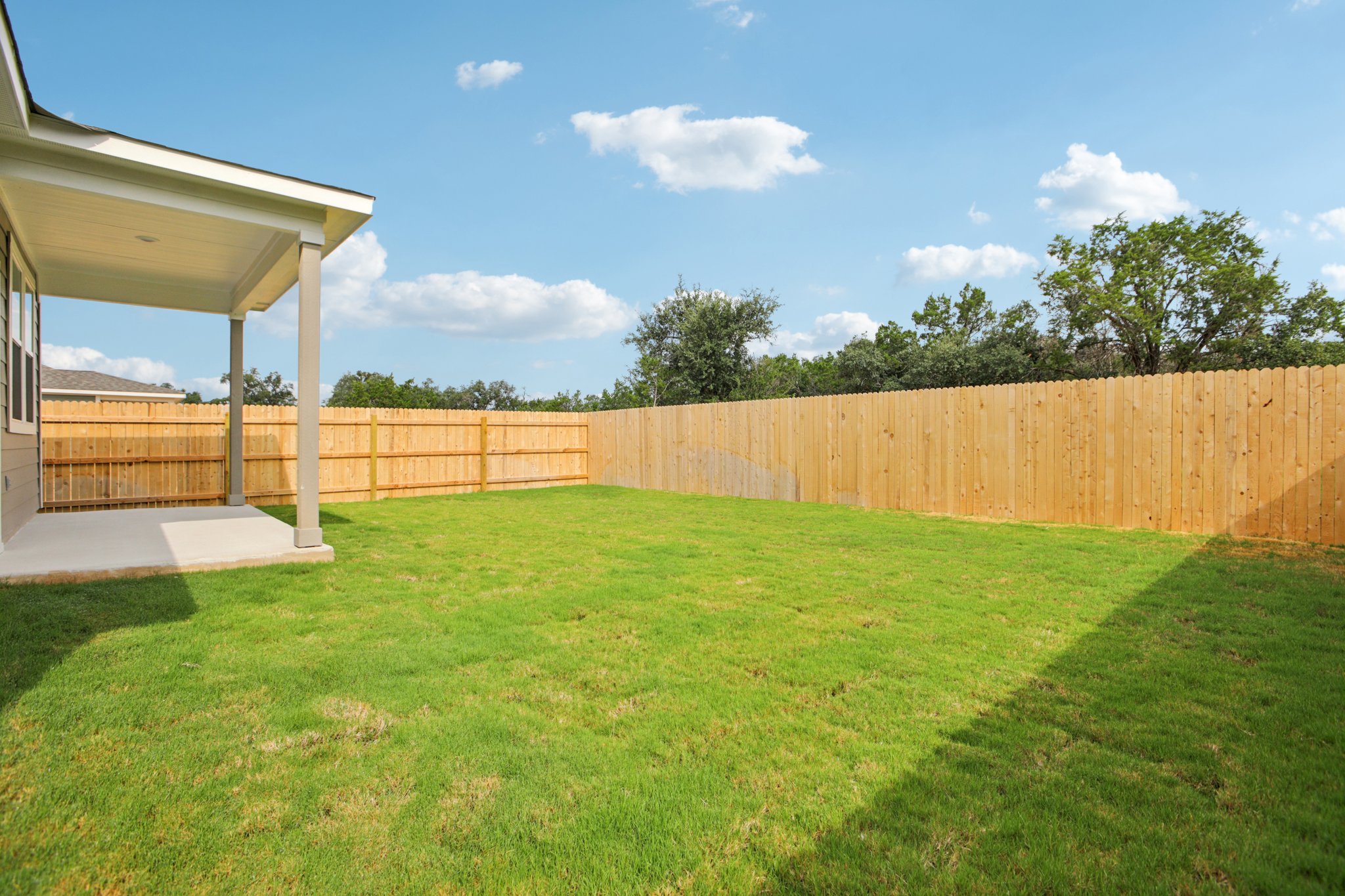 A fenced in yard with a wood fence and trees in the background.