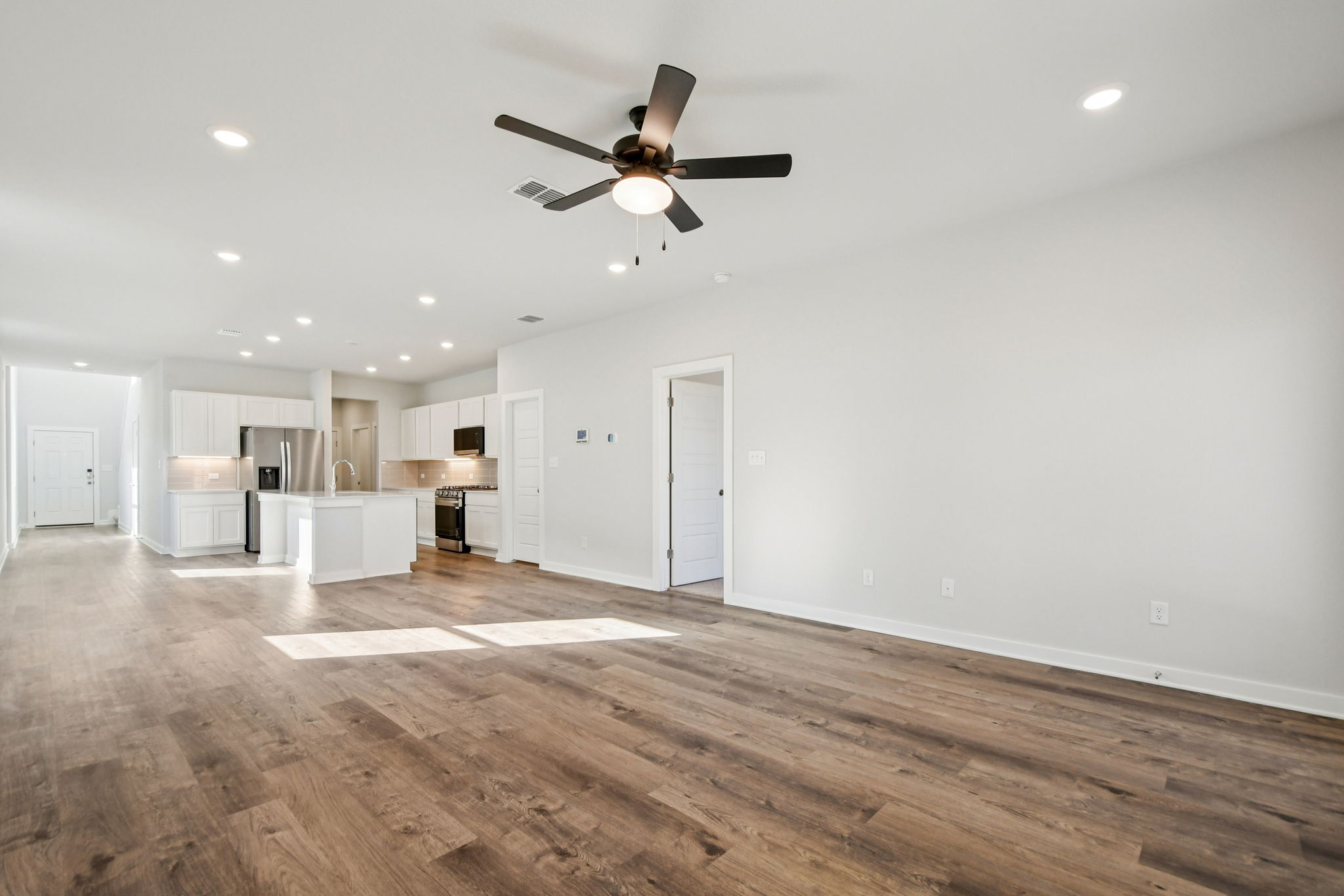 A large empty room with a ceiling fan and a wood floor.