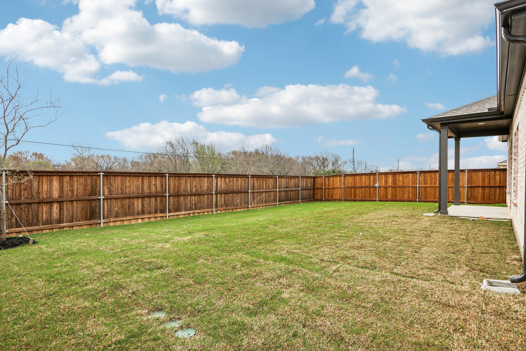 A fenced in yard with a wood building and trees in the background.