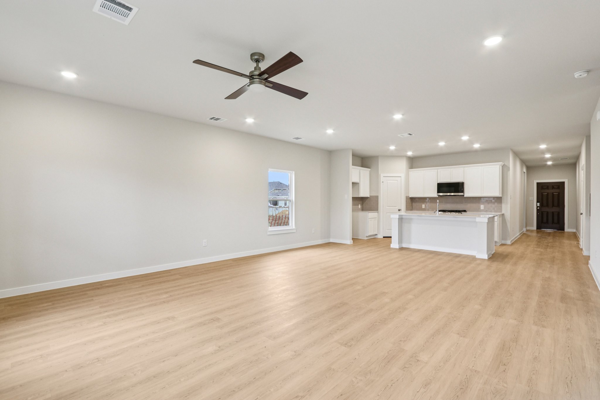 A large empty room with a wood floor and a ceiling fan.