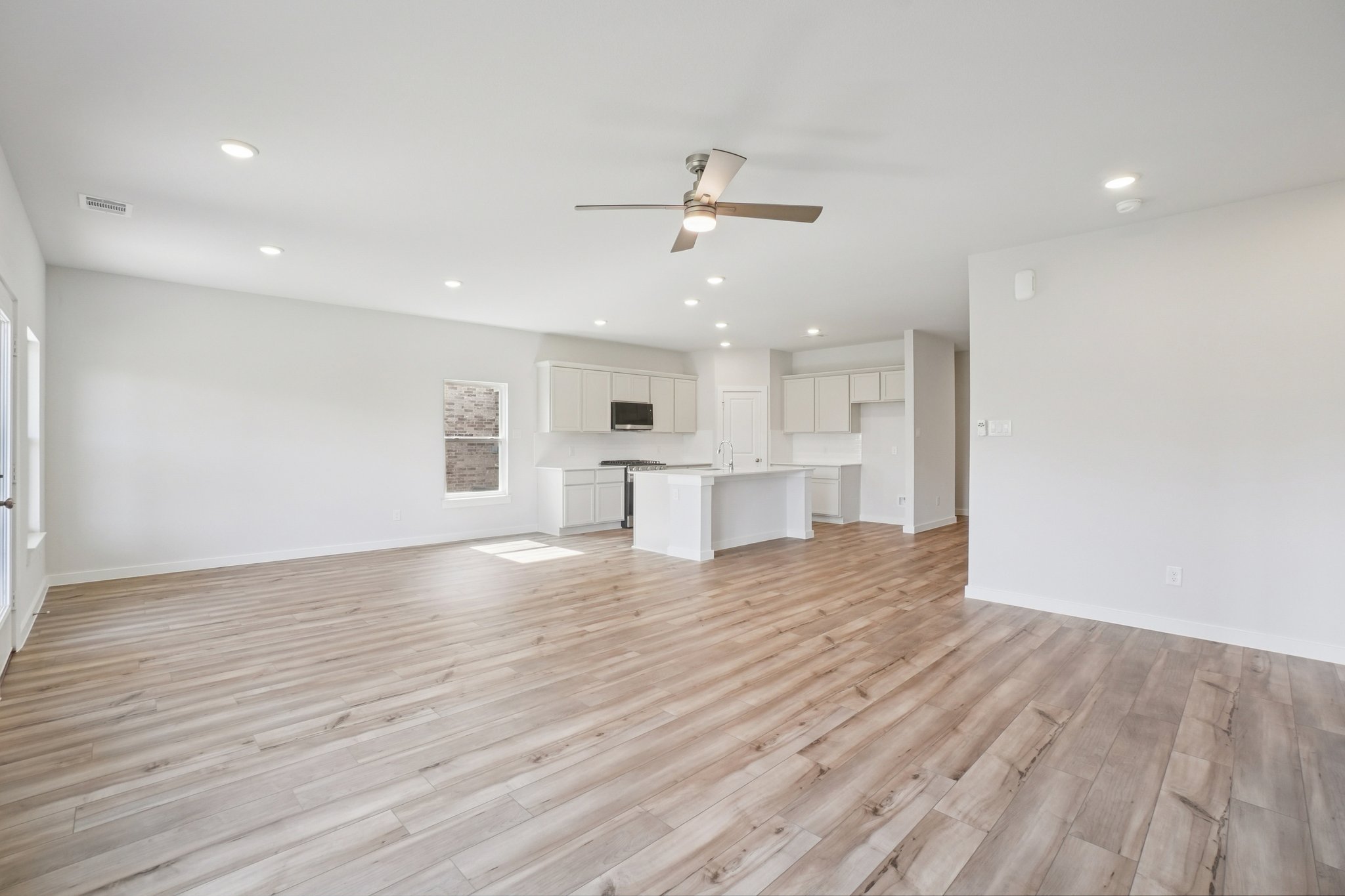 A large empty room with a wood floor and a ceiling fan.