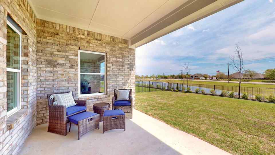A brick building with a patio and chairs and a grass yard.