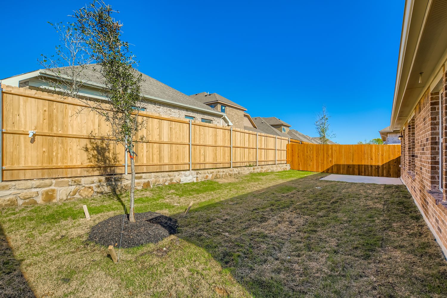 A fenced in yard with a tree and a house in the background.