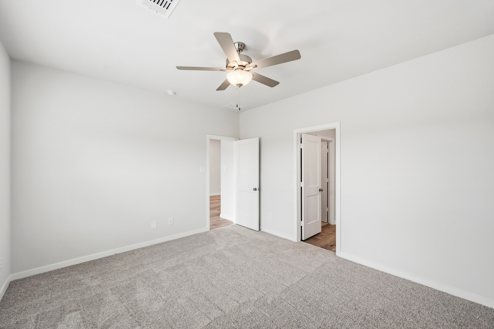 A room with a ceiling fan and a carpet.