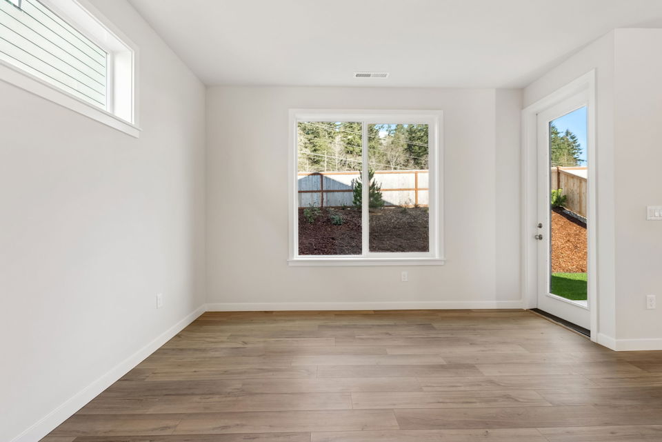 A room with a wood floor and a window with a view of the yard and a wood floor.