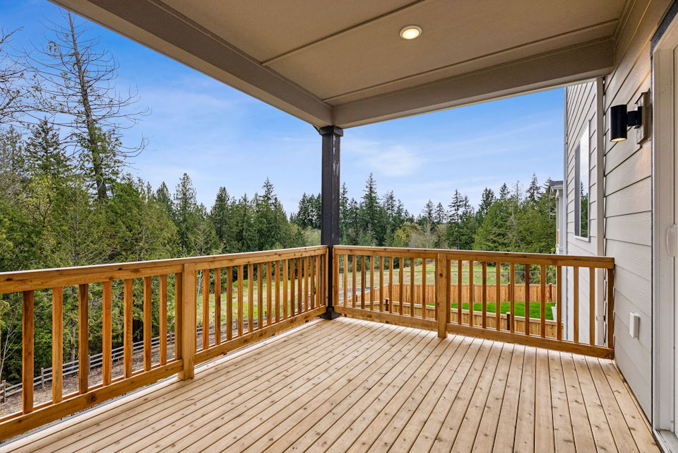 A deck with a wood railing and trees in the background.