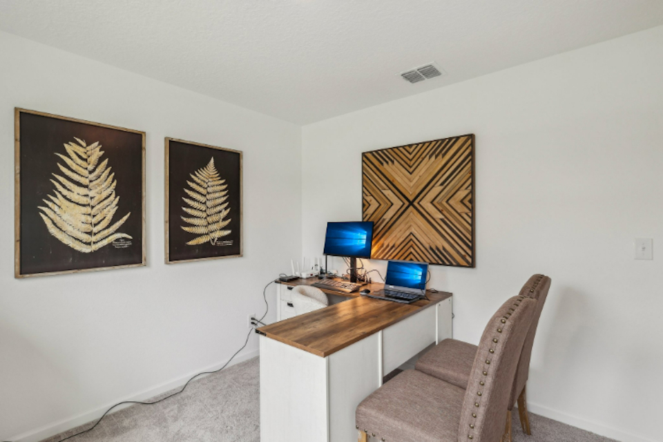 A desk with a computer and a chair in a room with pictures on the wall.